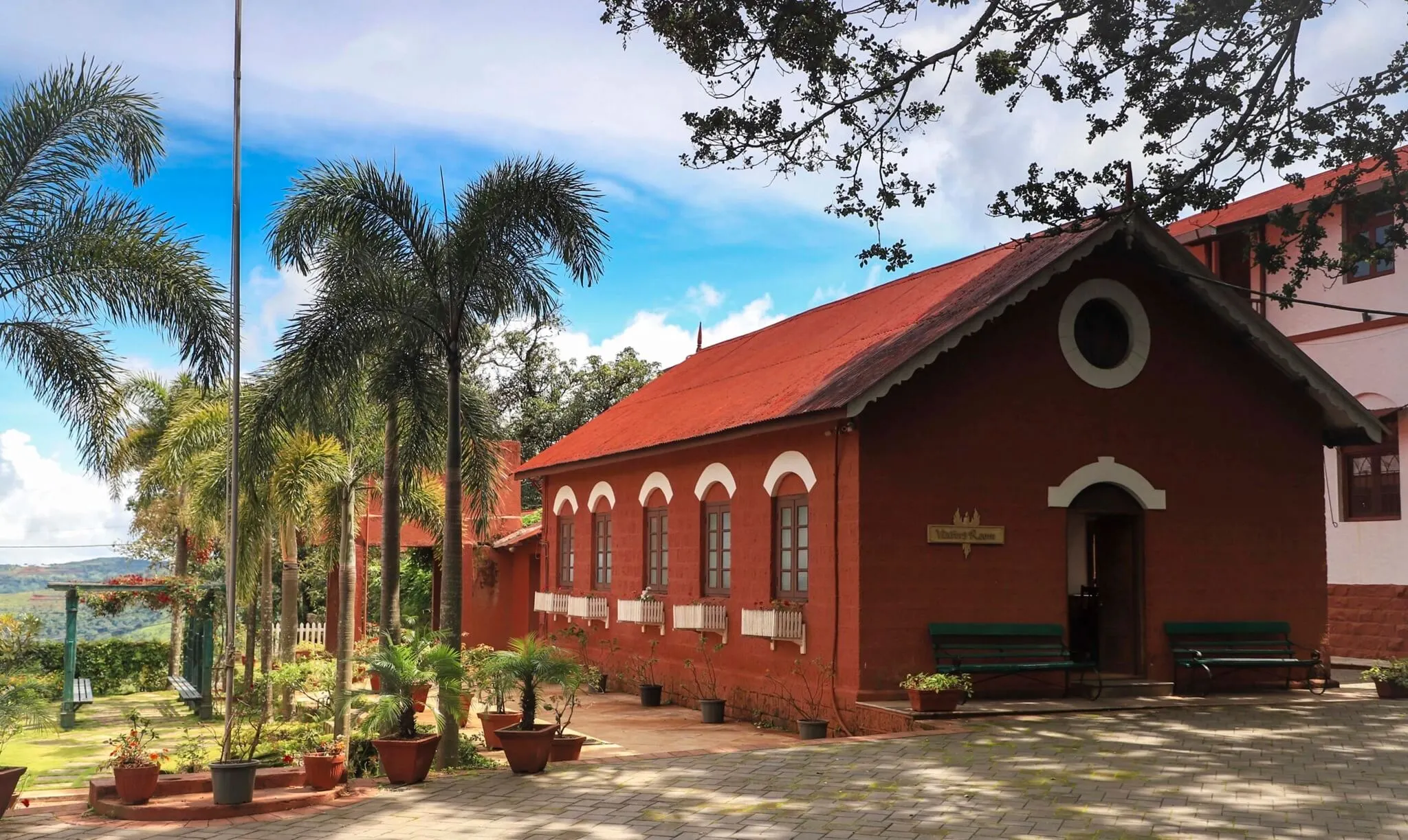 The red laterite Visitors' Room building at St. Peter's School, Panchgani, with palm trees and the Sahyadri hills behind